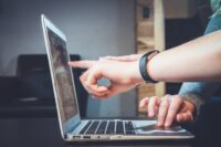 Foto: Seitenansicht von einem Laptop, eine Hand zeigt auf den Bildschirm